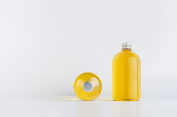 Set of two transparent plastic low thick bottles standing and lying with orange liquid, oil or cosmetic produce and silver cap, mockup on white background,  front and top view.