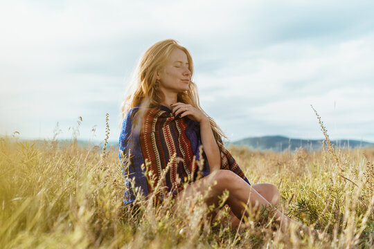 in the field sits and meditates a girl in loose hair in an ethno cape. High quality photo
