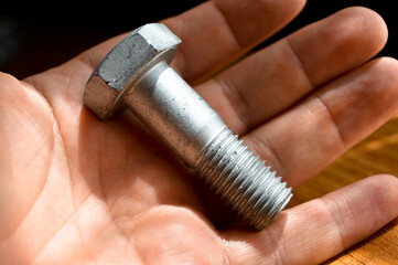 Galvanized metal with metric bolt and hand, isolated on brown walnut wood