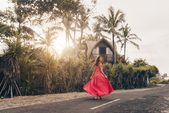 In Bali on the tarmac past the villa and palm trees in a long bright dress goes looking over the shoulder of the brunette. High quality photo