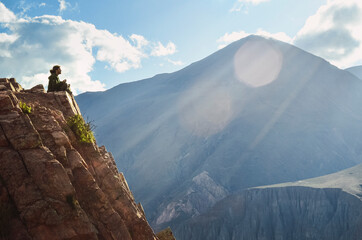 Man meditating in a mountain with sun reflections and cloudy sky. Iruya, Salta, Argentina. Yogi in landscape