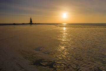 Fototapeta premium Winter landscape at the Lighthouse Paard van Marken Netherlands. On a cold day, temperature -7 degree during sunset. The IJsselmeer is frozen and by strong wind the shore was covered with ice