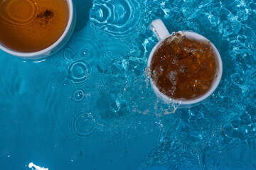 Two cups of tea in blue splashing water