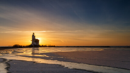 Winter landscape at the Lighthouse Paard van Marken Netherlands. On a cold day, temperature -7 degree during sunset. The IJsselmeer is frozen and by strong wind the shore was covered with ice