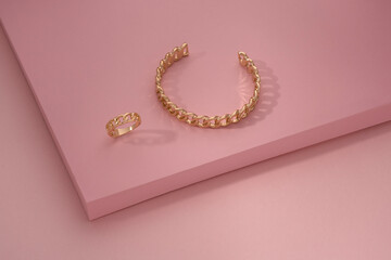 Chain shape golden bracelet and ring on pink background