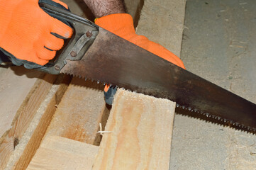 close-up - a man in gloves is sawing a wooden board with a saw