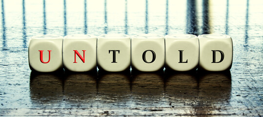 Concept of dices with letters forming word "told" or "untold" 	