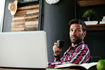 Young businessman working on laptop and drinking coffee in his office. Businessman on coffee break.