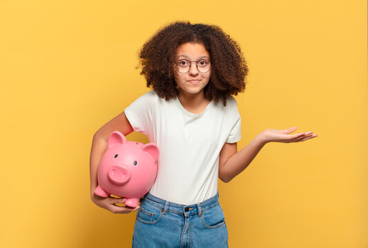 pretty afro teenager smiling with a happy, confident expression with hand on chin, wondering and looking to the side. savings concept