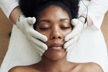 A dark-skinned model lies on the couch at the beautician and receives a microcurrent massage....
