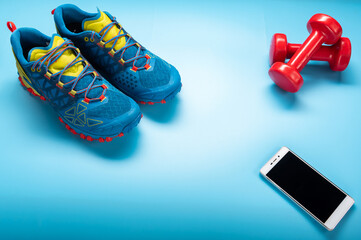 Blue running shoes on a blue background. Blue sneakers and red dumbbells. Smartphone and dumbbells.