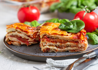 Italian lasagna with tomato sauce and cheese served with tomatoes and spinach, light concrete background. Homemade vegetarian lasagna.