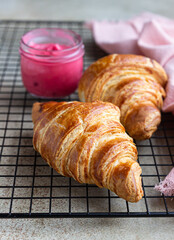 Fresh crispy croissants with pink honey on black metal grille, concrete background.