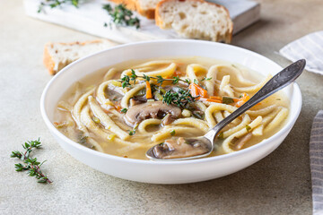 Vegan noodles soup with mushrooms and vegetables served with thyme, light concrete background.
