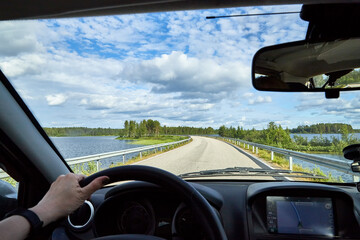 Car salon, steering wheel, hand of woman and view on nature landscape. Road, forest, blue sky, white clouds at sunny day. Concept of single trip of female traveller and driver during coronavirus