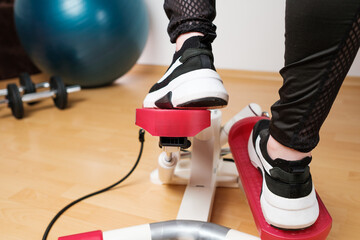 Back view on the woman feet in sneakers doing exercising on the twist stepper or stair stepper...