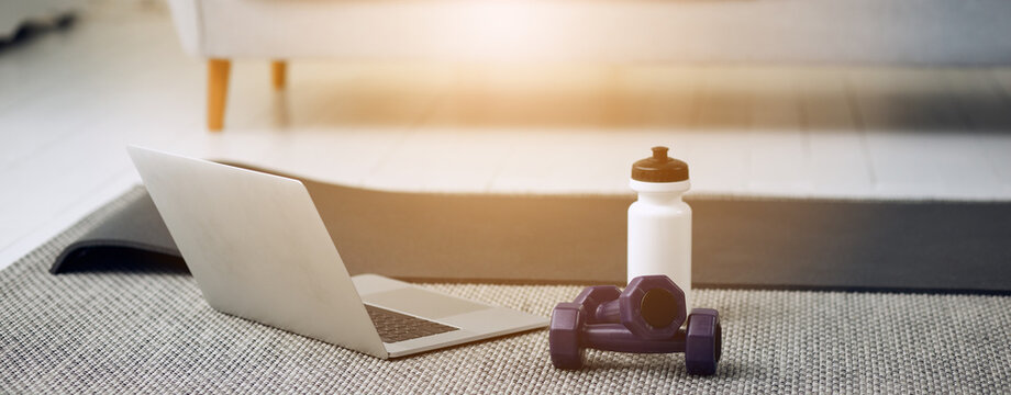 Equipment for training at home. Cropped photo of dumbells, laptop and bottle of water.