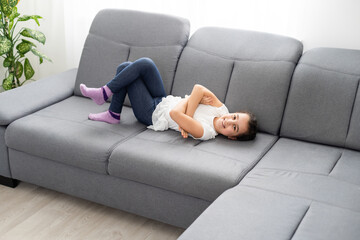 Brunette little girl in yellow blouse on a couch at home.