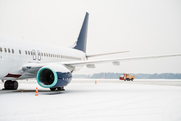 Side view of a passenger plane. A snowplow clearing snow from the runway is visible in the back.