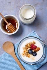 Healthy breakfast. Glass bowl with organic yogurt, fresh raspberries and blueberries, nuts and honey, on a textured wooden background