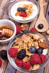on the rustic wooden background, tasty and healthy breakfast with yogurt, cereals, dried fruit, raspberries, blueberries and blackberries, bowl with forest honey.