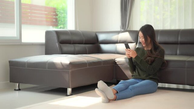 A pretty young woman sitting on the floor holding her smartphone laughs at what she sees.