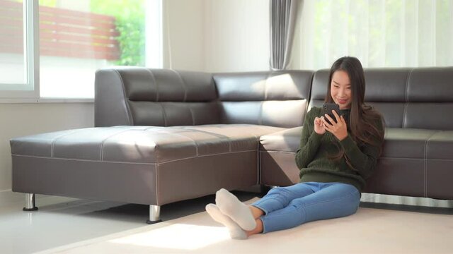 A cute young woman sitting on the floor enjoys interacting with her smartphone. Title space