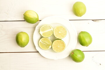 A few whole and halves of tasty organic lime on a white plate, on a painted wooden table.