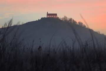 The chapel 'Wurmlinger Kapelle' near Tuebingen and Rottenburg in Germany on a hill glowing red while sunrise with a meadow in the foreground