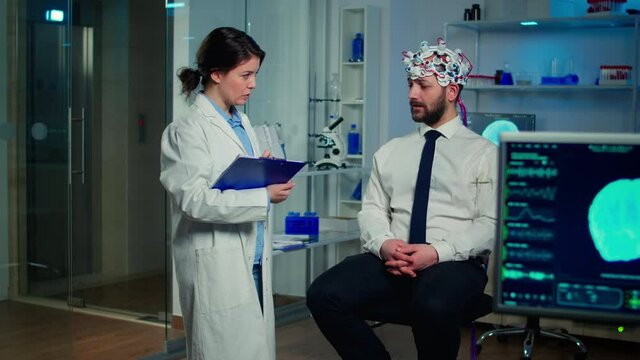 Medical doctor talking about symptoms of disease during investigations using high tech brainwave scanning headset. Researcher analysing health status of man patient, brain functions, nervous system