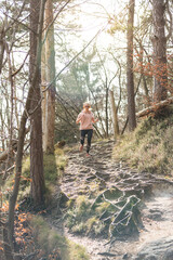 Naklejka na ściany i meble Active sporty woman listening to the music while running in autumn fall forest. Female runner training outdoor. Healthy lifestyle image of young caucasian woman jogging outside.
