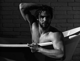 Guy with wet hair sitting in bath tub. Hygiene and healthcare. Sexy man with muscular body in...