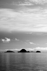 Naklejka na ściany i meble Black and white seascape with feathery clouds and a group of small islands in the horizon