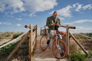 Adult man wearing face mask sitting in orange bike and using his phone.