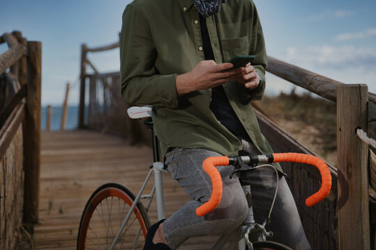 Unrecognized man sitting in cool orange bike in the coast and using his phone.