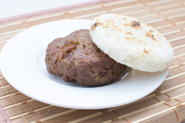 Seasoned meatloaf served with corn arepa on white wooden background