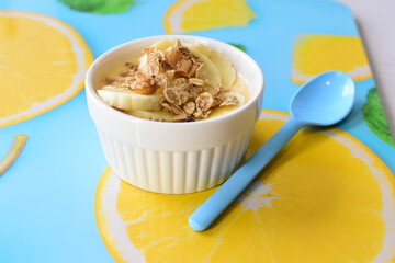 Chopped banana with granola in white bowl, on wooden background printed with fruits