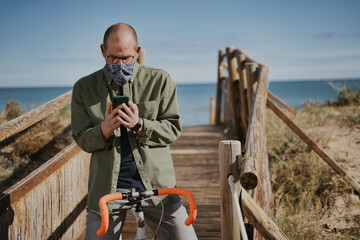 Adult man wearing face mask sitting in orange bike and using his cellphone.