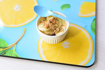 Chopped banana with granola in white bowl, on wooden background printed with fruits