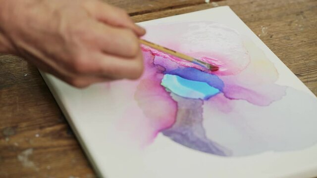Fluid Art. Abstract colorful painting. Close up of female artist pours water to canvas and uses paintbrush to distribute it