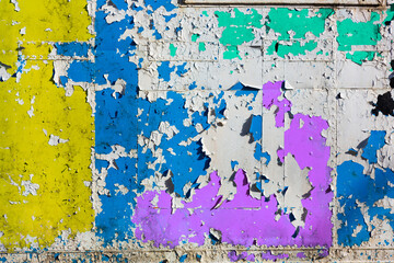 Grungy weathered metal surface with white old paint peeling off exposing old blue, magenta, cyan and yellow paint