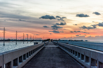 Fototapeta na wymiar Cloudy sky at sunrise in Islamorada, Florida keys with colorful sky by overseas highway road of Gulf of Mexico with power lines and pedestrian bridge, people fishing