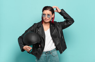 young attractive red hair woman feeling puzzled and confused, scratching head and looking to the...
