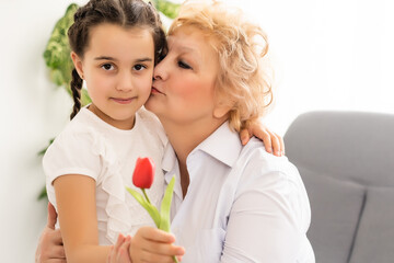 Fototapeta na wymiar Congratulations concept. Congratulations on the holiday. The granddaughter gives flower to her grandmother on March 8th. International Women's Day. Grandmother and granddaughter with flower