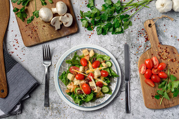 Fresh salad with lettuce tomato cucumber mushroom cheese and parsley top view over gray stone table 