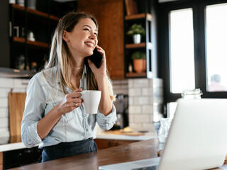 Beautiful woman drinking coffee and using the phone in the kitchen. Young woman talking to the phone.