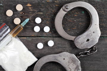 Syringe with cocaine and police handcuffs on a dark wooden background, top view