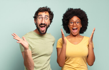 multiracial couple of friends feeling happy, excited, surprised or shocked, smiling and astonished...