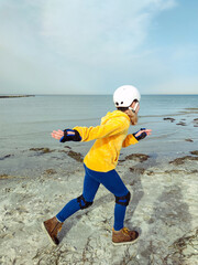 Happy child girl in yellow pullover in helmet and inline protective equipment running and having...