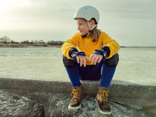 Portrait of pretty teenager girl in yellow pullover, helmet and inline protective equipment posing...